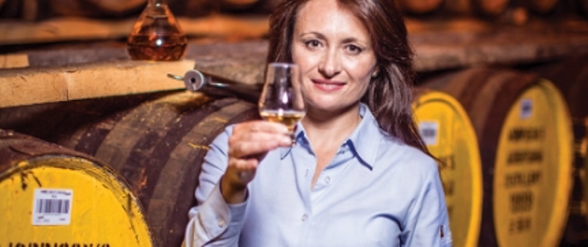 Woman holding whisky glass in front of whisky barrels