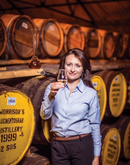 Woman holding whisky glass in front of whisky barrels